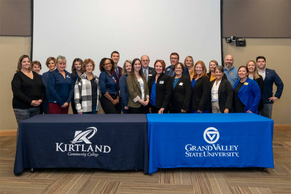 Kirtland Community College and Grand Valley State University standing behind two tables side by side